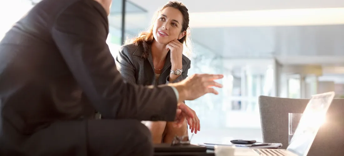 Alt text: Two business professionals talking at a table in a bright office